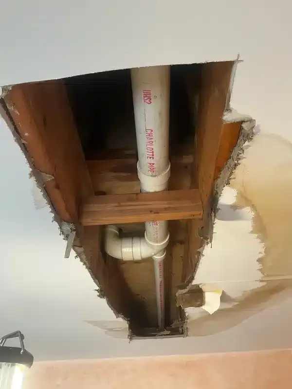 Exposed ceiling plumbing repair showing PVC drain pipe replacement and water damage in a West Milford residence.