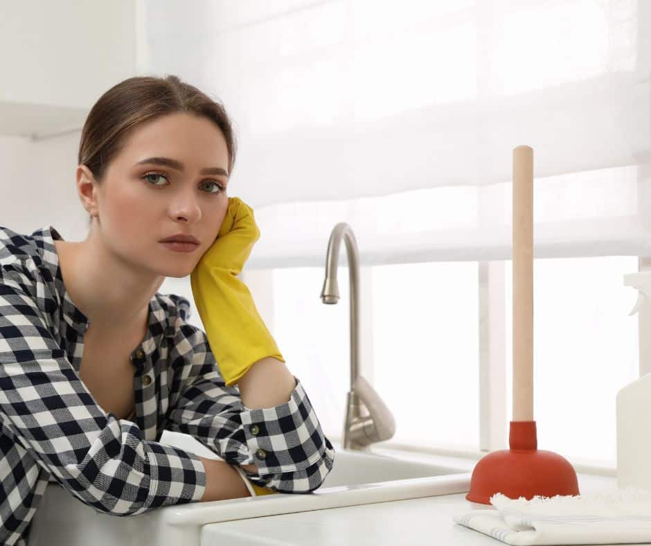 A woman in her kitchen experiencing signs you need drain cleaning.