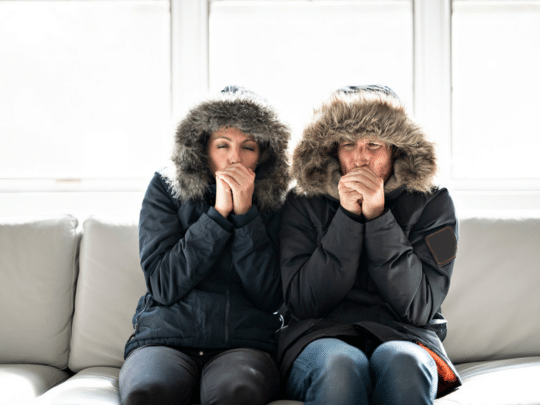 couple on couch wearing winter jackets because heater is broken